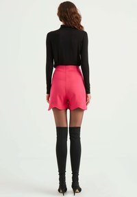 Åtsittande svart långärmad topp och rosa shorts med vågig fåll. Modellen bär svarta knähöga klackstövlar som framhäver en välsittande silhuett.