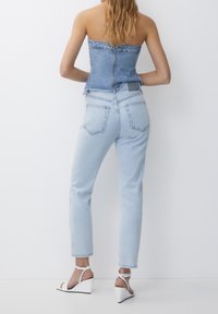 Top de tubo de mezclilla en azul claro con cremallera en la parte posterior, combinado con jeans de tiro alto en azul claro. Sandalias de cuña blancas con tirantes en el tobillo.
