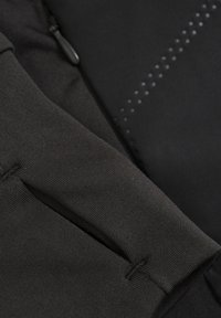 Svart atletisk tyg som visar en texturerad väv och släta sektioner. Har en ficka med dragkedja och subtila prickade mönsterdetaljer.