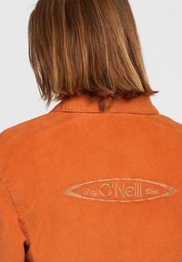 Giacca in corduroy arancione con colletto e logo O'Neill ricamato sul retro. La texture è a coste e il design è classico.
