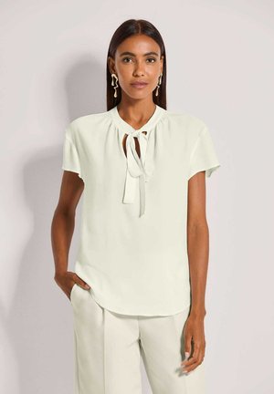 Lichtgroene blouse met korte mouwen, een ronde hals en een strikdetail aan de voorkant. Gemaakt van gladde stof met een losse pasvorm.