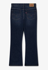 Ciemnoniebieskie dzwony z denimu z standardowym pasem, tylnymi kieszeniami z charakterystycznym zakończeniem w kształcie litery V oraz skórzaną naszywką z logo z tyłu.