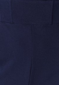 Tamsiai mėlynos spalvos audinys su lygia tekstūra, su vertikaliomis siūlėmis ir struktūruotu liemens diržu. Paprastas, pritaikytas dizainas be papuošimų.