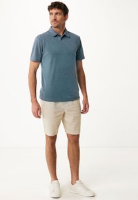 Herrblå polo skjorta med korta ärmar, med en krage; kombinerad med beige shorts och vita sneakers. Enkel design, avslappnad passform.