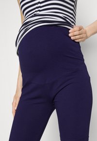 Grūtniecības legingi tumši violetā kokvilnā, ar plašu, elastīgu jostasvietu un gludu, pieguļošu dizainu, kas sniedzas līdz pusstilbam.