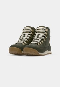Bottes de randonnée vertes avec une tige texturée, un bout renforcé et des accessoires en or. Elles sont équipées de lacets blancs et d'une semelle extérieure en caoutchouc brun pour une meilleure traction.