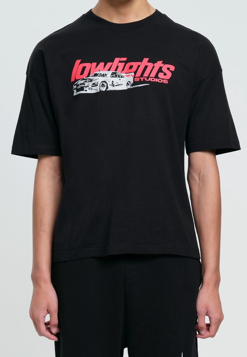 T-shirt noir à manches courtes avec texte rouge "lowlights studios" et un graphisme blanc d'une voiture de course vintage sur la poitrine.