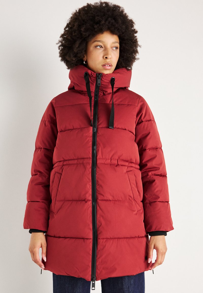 Red puffer coat with a high collar, black zip closure, and horizontal quilting. Features side pockets and black accents on cuffs.