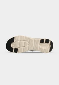 Semelle de chaussure avec motif de bande de roulement beige et noir, montrant une adhérence texturée et le nom de la marque Skechers au niveau du talon.