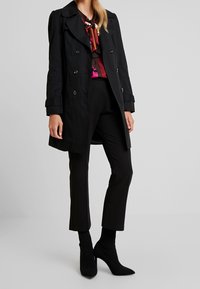 Czarny płaszcz trencz o kroju dwurzędowym, z dużym kołnierzem i długimi rękawami. Zestawiony z dopasowanymi czarnymi spodniami i czarnymi botkami na wysokim obcasie.