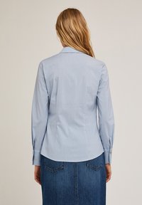 Camisa de botones de rayas azul claro, con mangas largas y un ajuste entallado, que presenta un cuello en pico y detalles en los puños. Combinada con una falda de mezclilla.