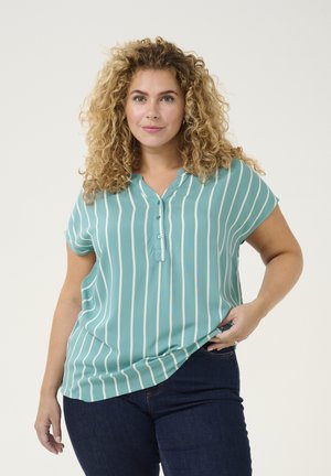 Blouse rayée turquoise à manches courtes, avec des boutons et une coupe décontractée. Le tissu semble léger et lisse, associé à un jean noir.