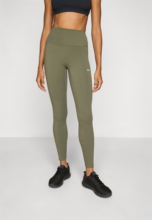 Høyt liv, olivengrønne tights med en jevn tekstur og en liten hvit Nike-logo på låret. Kombinert med svarte treningssko.