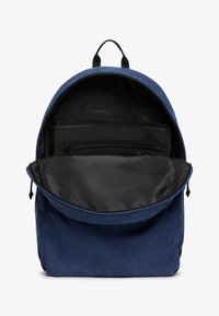 Niebieski plecak z tkaniny o zaokrąglonym kształcie, czarnym wnętrzu, wieloma przegrodami i zamykaną na zamek kieszenią z przodu. Wyposażony w uchwyt na górze.