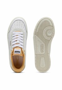 Baskets blanches avec des accents jaunes, comportant une tige en cuir et en daim, un bout arrondi, des lacets plats blancs, et une semelle en caoutchouc texturée.