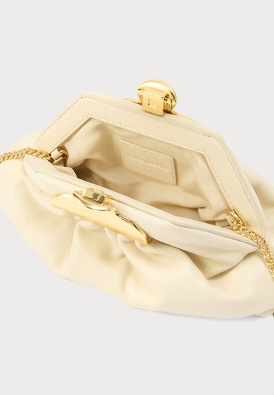 Κρεμ δερμάτινο τσαντάκι χειρός με χρυσό μεταλλικό κούμπωμα και αλυσίδα για τον ώμο. Το εσωτερικό είναι επενδεδυμένο με απαλό ύφασμα, με διακριτική υφή.