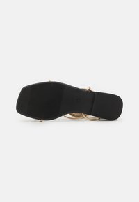 Semelle noire d'une chaussure avec une texture de grip, présentant des accents dorés courbés au-dessus de la semelle. Forme plate et rectangulaire avec des lignes épurées.