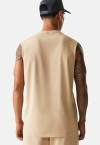 Maglietta senza maniche beige in morbido cotone. Tessuto liscio con una vestibilità rilassata e orlo piatto. Presenta un classico collo rotondo e dettagli sulla schiena.