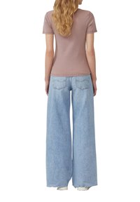 Aansluitend ribgebreid T-shirt met korte mouwen in mauve, gecombineerd met lichtblauwe wijde jeans met achterzakken en subtiele stikdetails.