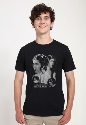 Giovane uomo che indossa una maglietta nera con molteplici ritratti in bianco e nero della Principessa Leia e testo "Leia Organa I Love You."