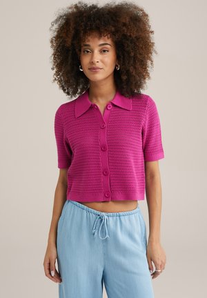 Cardigan en tricot fuchsia à manches courtes avec fermeture à boutons et col classique, associé à un pantalon bleu clair avec cordon de serrage.