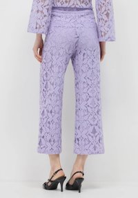 Pantalons larges en dentelle violette avec un motif floral, dotés d'une taille haute et d'une longueur raccourcie. Associés à des sandales à talons noirs.