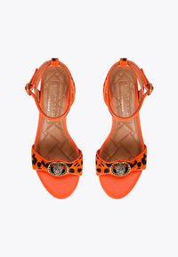 Pomarańczowe sandały na wysokim obcasie z paskami w leopardzi wzór, z elementami w odcieniu złota oraz teksturowaną wkładką. Posiadają pasek wokół kostki dla dodatkowego wsparcia.