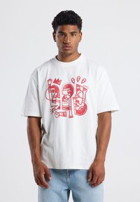 White cotton t-shirt featuring red abstract graphic design. Short sleeves, round neckline, relaxed fit, and soft texture.