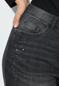 Donkergrijze denim jeans hebben een nauwsluitend ontwerp met een klein voorvak en decoratieve versieringen van verschillende kralen aan de zijkant.