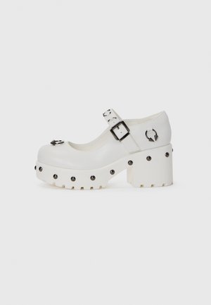 White platform shoes with a rounded toe, buckle strap, and circular studs. Textured sole with a slight heel and decorative hardware detail.