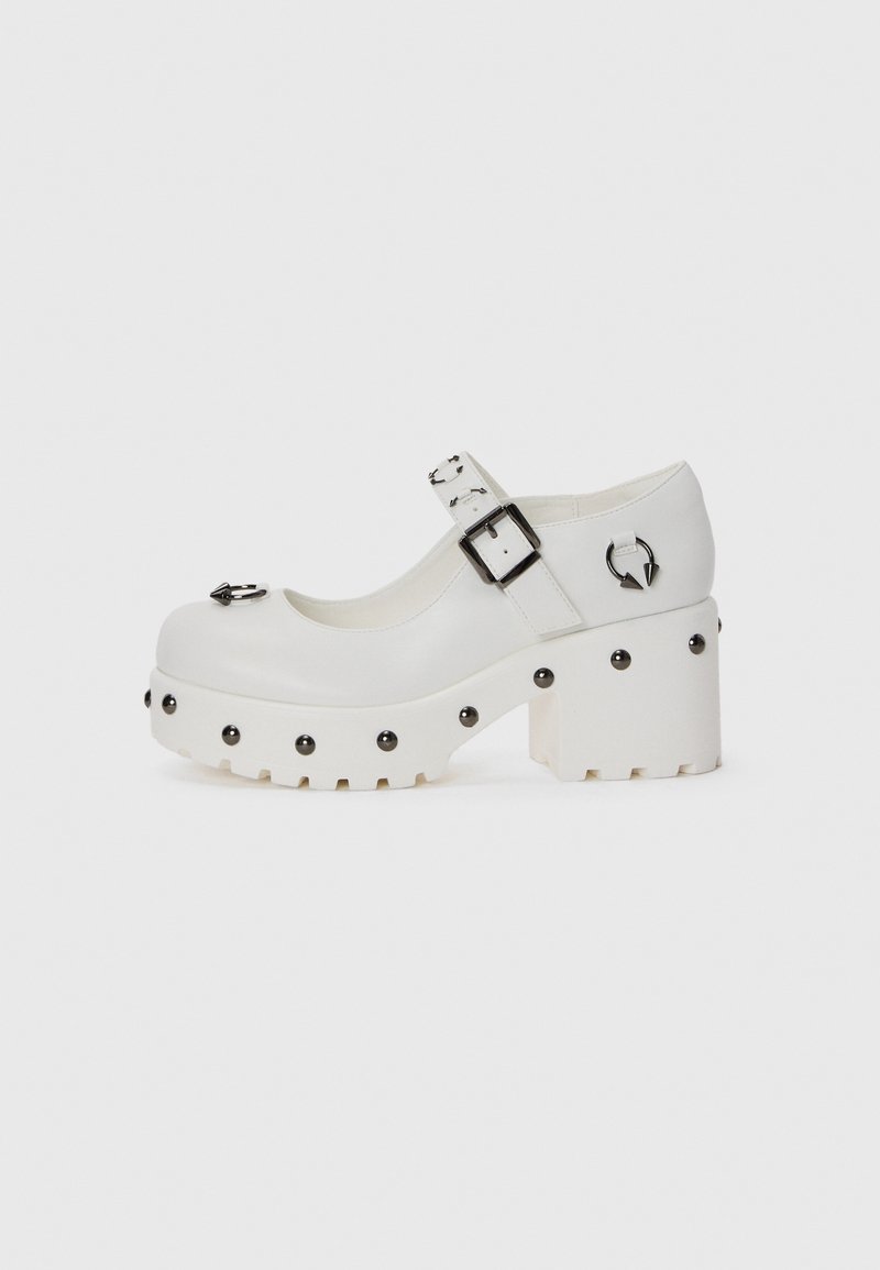 White platform shoes with a rounded toe, buckle strap, and circular studs. Textured sole with a slight heel and decorative hardware detail.
