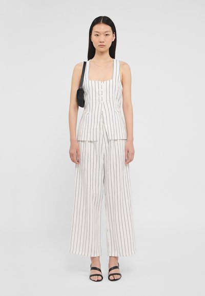 Ensemble en deux pièces comprenant un haut ajusté à encolure carrée avec des rayures noires verticales, associé à un pantalon à jambes larges, également rayé. Accessoirisé avec un petit sac noir.