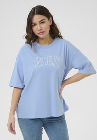 T-shirt en coton bleu clair à manches courtes, arborant le mot "BIEN" brodé en lettres blanches sur le devant.