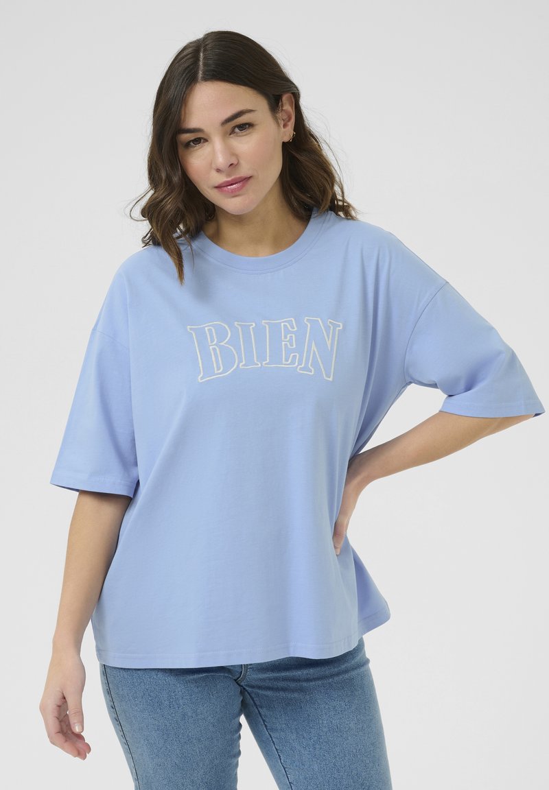 T-shirt en coton bleu clair à manches courtes, arborant le mot "BIEN" brodé en lettres blanches sur le devant.