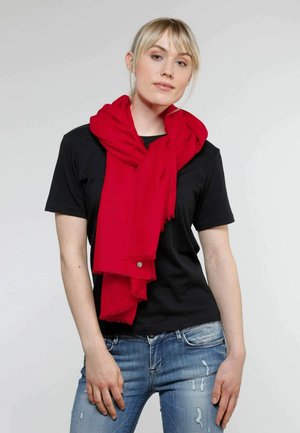 Sciarpa rossa con bordi sfilacciati, realizzata in morbido tessuto, indossata in modo rilassato attorno al collo sopra una maglietta nera, abbinata a jeans blu strappati.