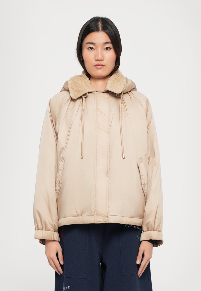 Doudoune de couleur beige clair, avec col en fausse fourrure, capuche à cordon de serrage et poches latérales ; texture lisse et coupe décontractée.