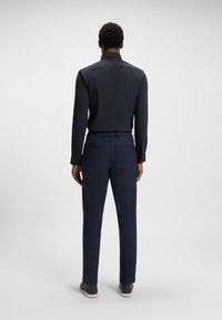 Marineblaues Langarmhemd mit strukturiertem Kragen, kombiniert mit marineblauen Hosen und lässigen Schuhen, von hinten betrachtet. Glatter Stoff, taillierte Passform.