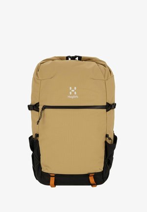 Sac à dos beige avec une surface texturée, accents noirs, poche zippée à l'avant et bretelles ajustables. Logo présent à l'avant.