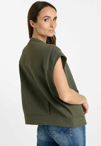 Maglia oversize di colore verde oliva, con texture, maniche corte e scollatura rotonda, abbinata a jeans in denim. Silhouette semplice e rilassata.