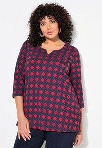 Top a righe blu navy e rosso con scollatura a V e maniche a tre quarti, caratterizzato da forme a diamante e testo in tutto il design. Tessuto dalla texture liscia.