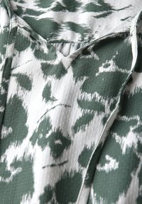 Tessuto a motivi verdi e bianchi con scollatura a V, caratterizzato da una combinazione di texture e un design astratto sottile.