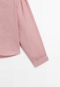 Manche longue d'une chemise en lin rose clair avec un poignet droit sur fond blanc.