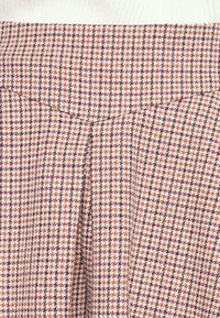 Geweven stoffen rok met een houndstooth patroon in tinten van oranje, bruin en wit, met plooien in de taille voor extra volume.