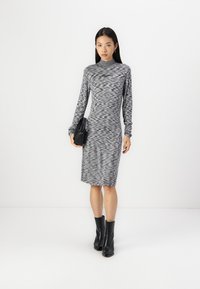 Pilkas ir juodas raštuotas ilgomis rankovėmis su aukštu kaklu, prigludusio silueto, siekiantis kelius, derinamas su juodais auliniais batais ir juoda rankine.