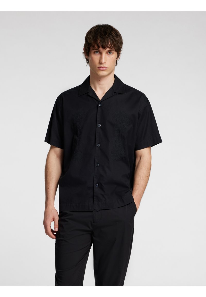 Camicia nera a maniche corte realizzata in tessuto leggero, con colletto, chiusura con bottoni e sottili dettagli tessuti sul petto.