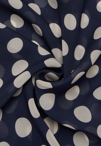 Dunkelblaue Stoff mit großen cremefarbenen Polka-Dots, der über eine glatte, leichte Textur verfügt und sanft gefaltet ist, um das Design und Muster zu zeigen.