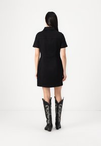 Vestido de ganga preto com mangas curtas, gola e um design ajustado, combinado com botas de cowboy altas pretas com bordados prateados.
