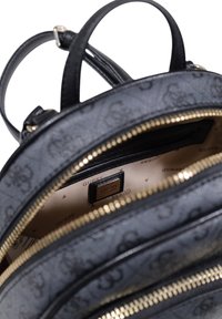 Mochila negra con textura y herrajes dorados, que cuenta con múltiples compartimentos con cremallera y un detalle de logo en el forro interior.