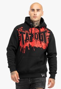 Melnā kapuce ar sarkano "TAPOUT" logotipu un plankumu dizainu, ar kangarū kapuci un auklu. Mīksta auduma, brīva piegriezuma.