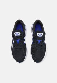 Schwarze Sportschuhe mit Obermaterial aus Mesh und Wildleder, weißen Streifen, blauen Akzenten und einem weißen Logo auf der Zunge. Schnürdesign für einen sicheren Sitz.